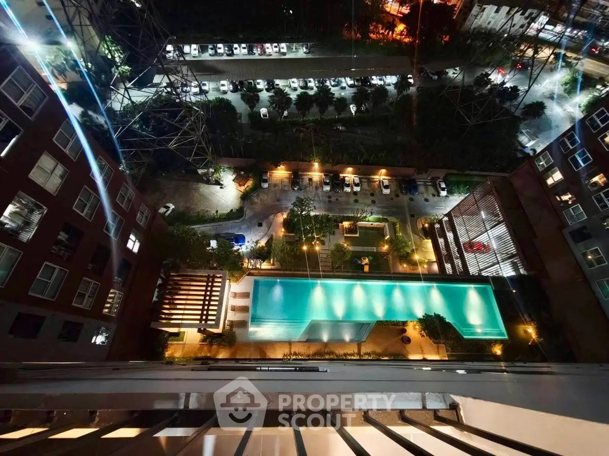 Stunning aerial view of illuminated pool and parking area in modern residential complex at night.