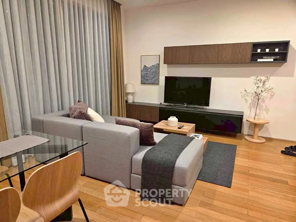 Modern living room with stylish furniture and wooden flooring, featuring a cozy gray sofa and a sleek TV setup.