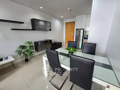 Modern dining area with sleek black chairs and glass table, adjacent to a stylish living room setup.