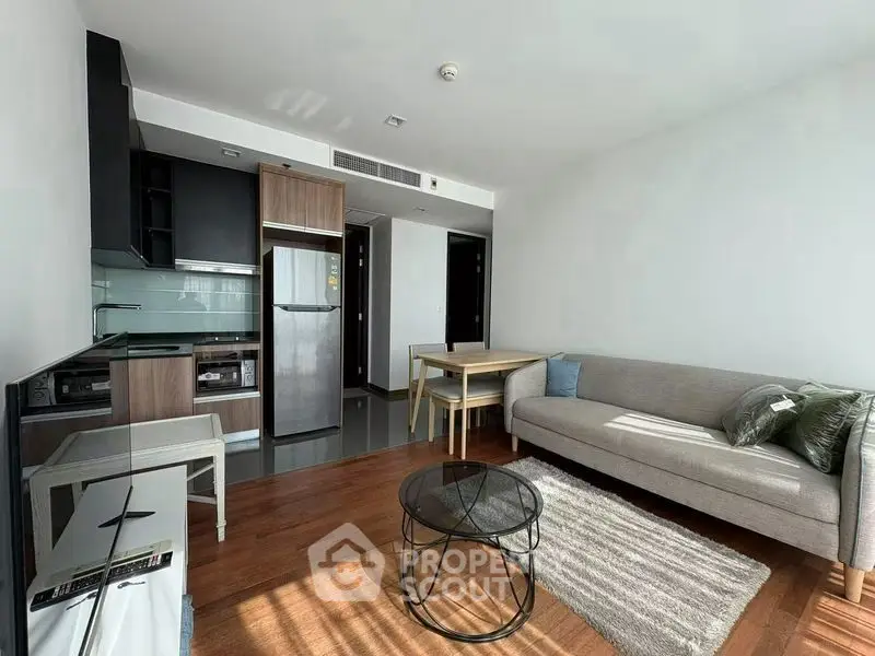 Modern living room with open kitchen, featuring sleek appliances and stylish furniture in a bright, airy space.