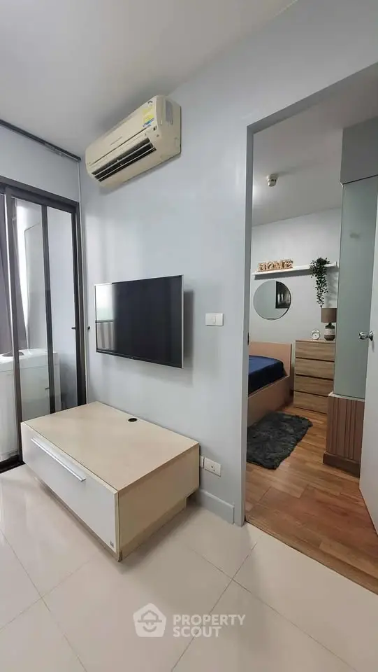 Modern apartment interior with wall-mounted TV and air conditioning, leading to a cozy bedroom.