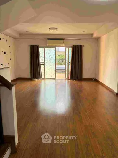 Spacious living room with wooden flooring and large windows for natural light.
