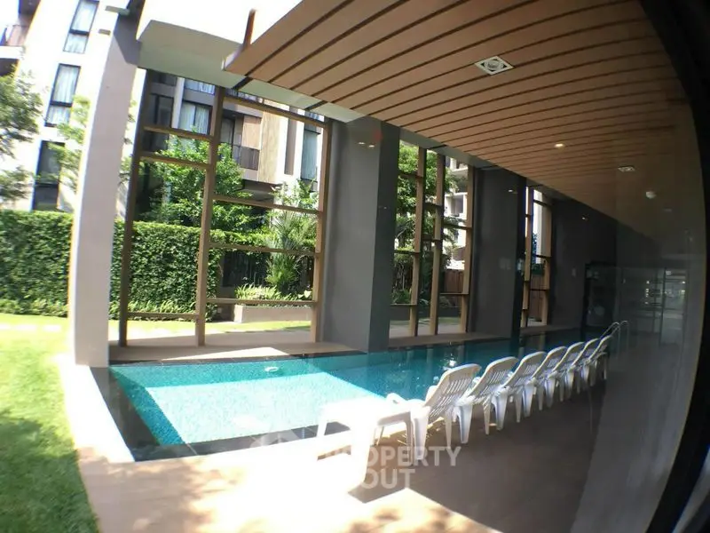 Luxurious modern pool area with stylish lounge chairs and lush greenery in a contemporary residential complex.