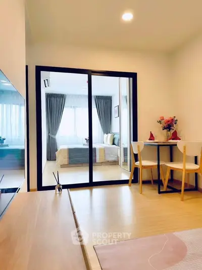 Modern open-plan living room with sliding glass doors leading to a cozy bedroom, featuring stylish decor and natural light.