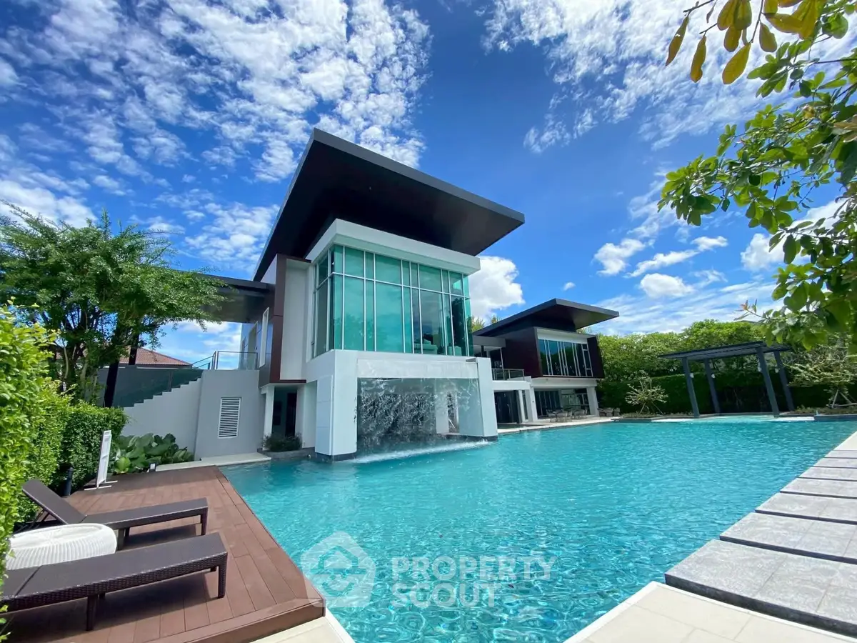 Luxurious modern villa with stunning pool and waterfall feature under a clear blue sky.
