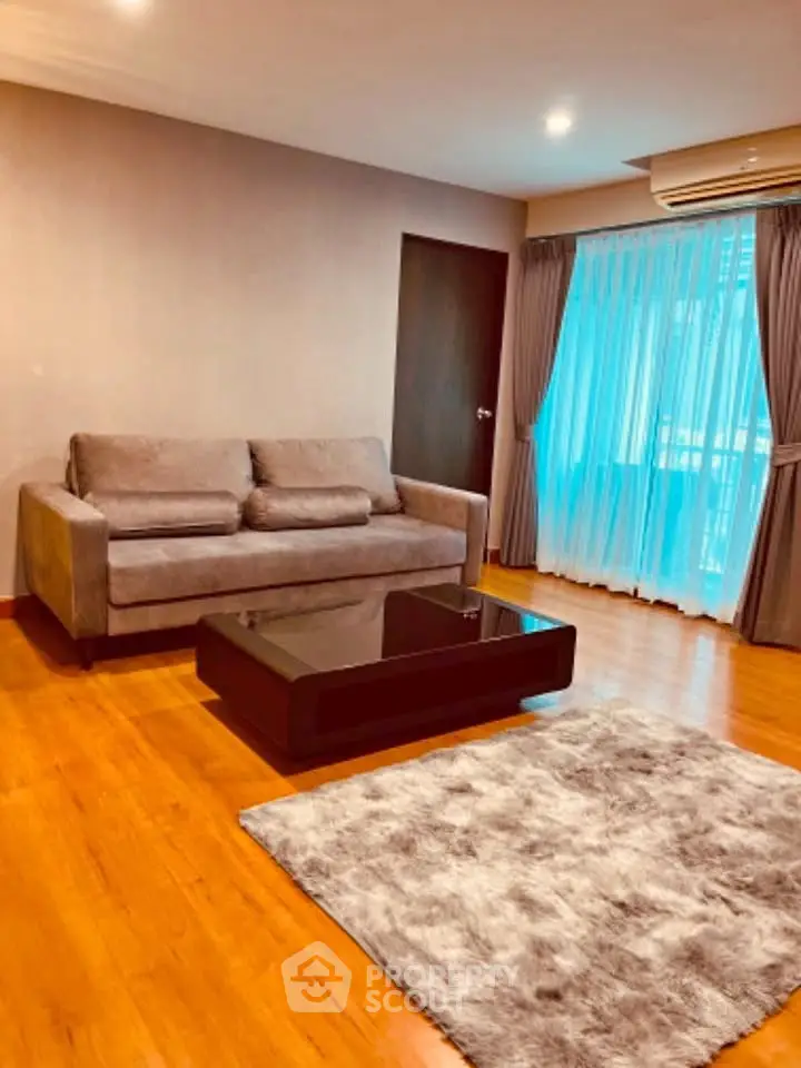 Spacious living room with modern sofa and elegant decor, featuring large windows and wooden flooring.