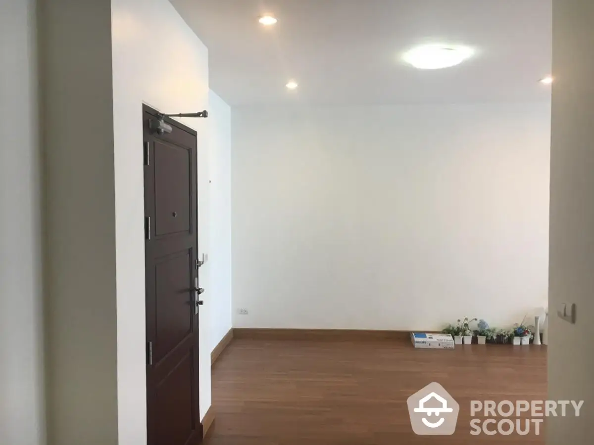 Spacious entryway with wooden flooring and minimal decor, leading into a bright and airy living space.