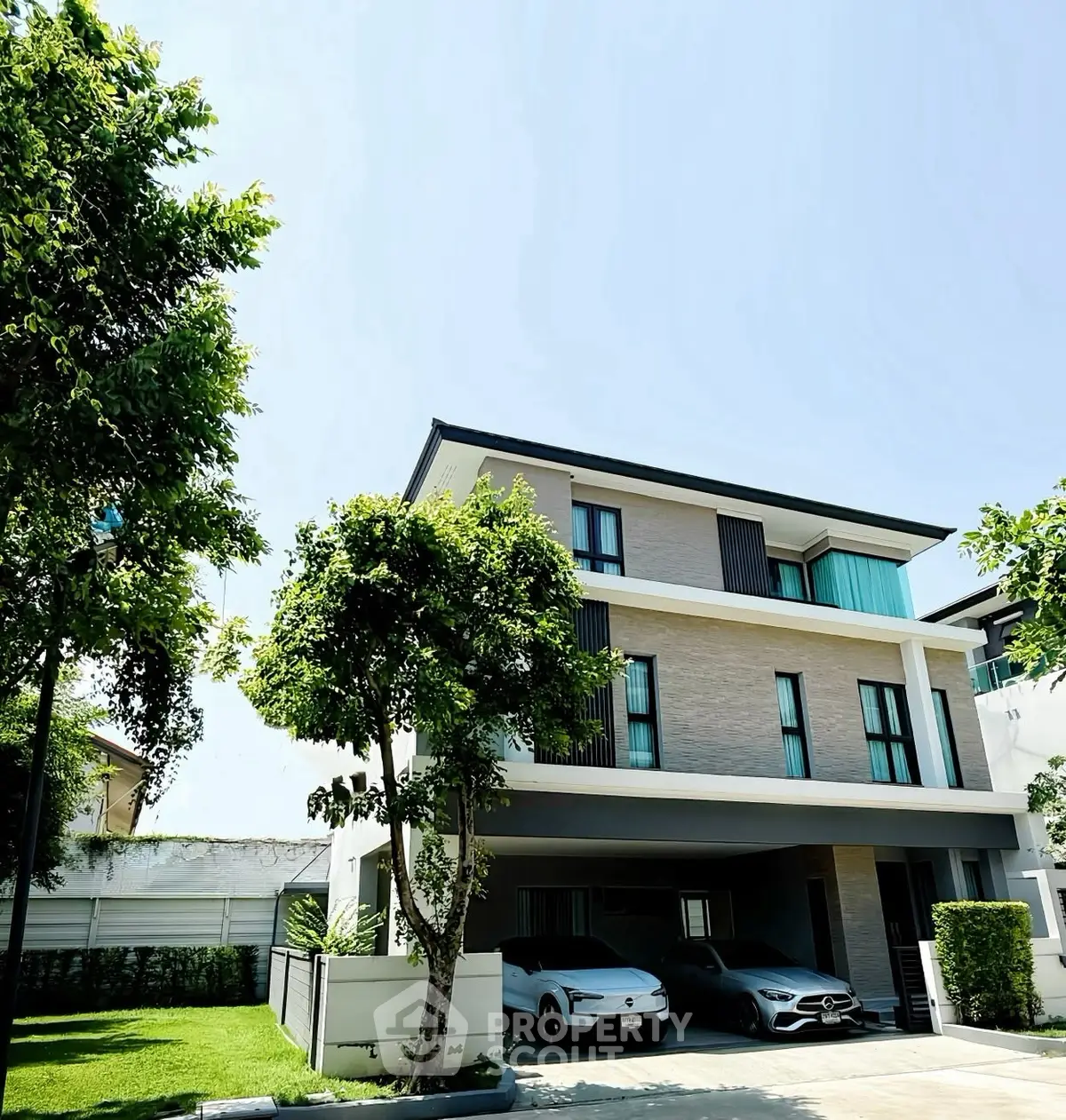 Modern three-story house with sleek design and two-car garage in a lush green neighborhood.