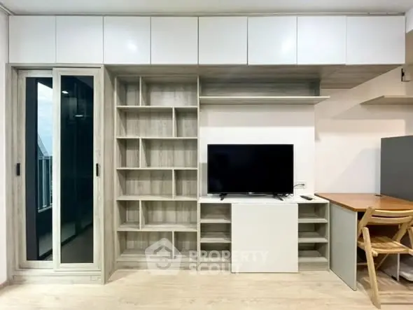 Modern living room with built-in shelves and TV, featuring a sleek balcony view.