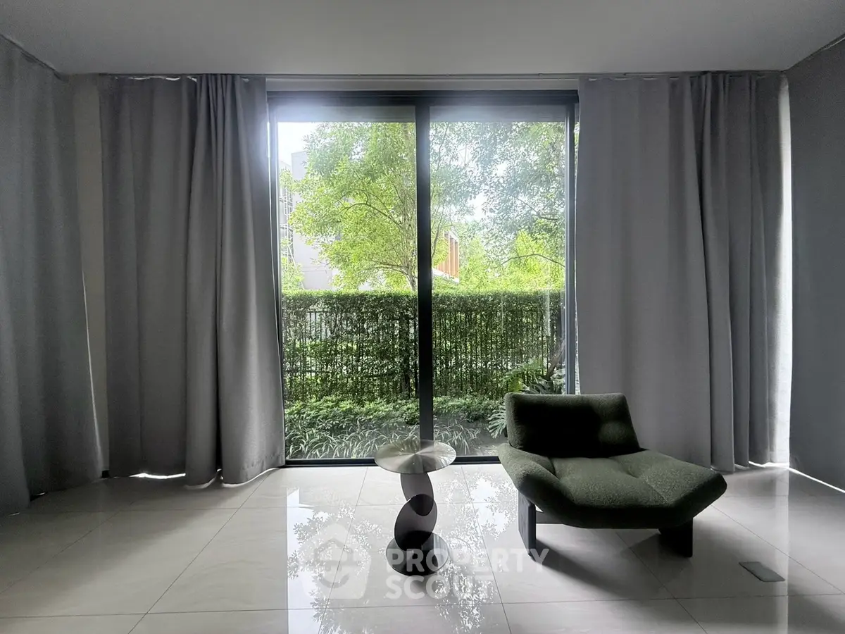 Modern living room with large window and stylish chair overlooking lush greenery.
