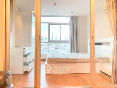 Modern bedroom with large windows and city view, featuring sleek furniture and wooden flooring.