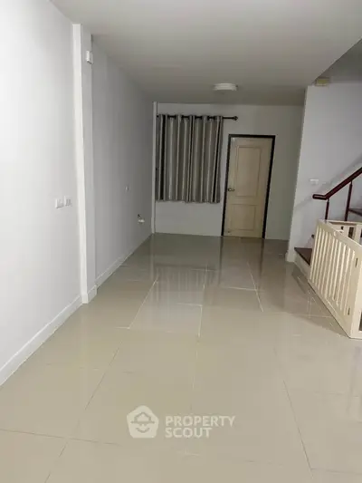 Spacious empty room with tiled flooring and staircase, ideal for customization.