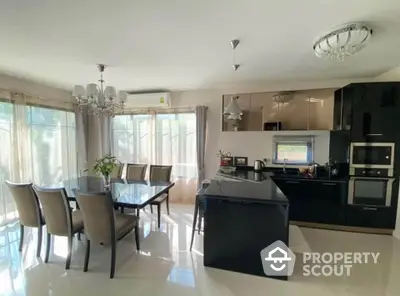 Modern kitchen with sleek black cabinets and elegant dining area, flooded with natural light.