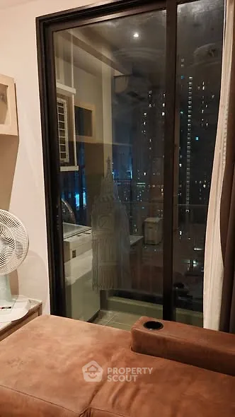 Cozy living room with city view through large glass door, featuring modern decor and comfortable seating.