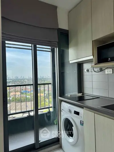 Modern kitchen with washing machine and city view from balcony in high-rise apartment.