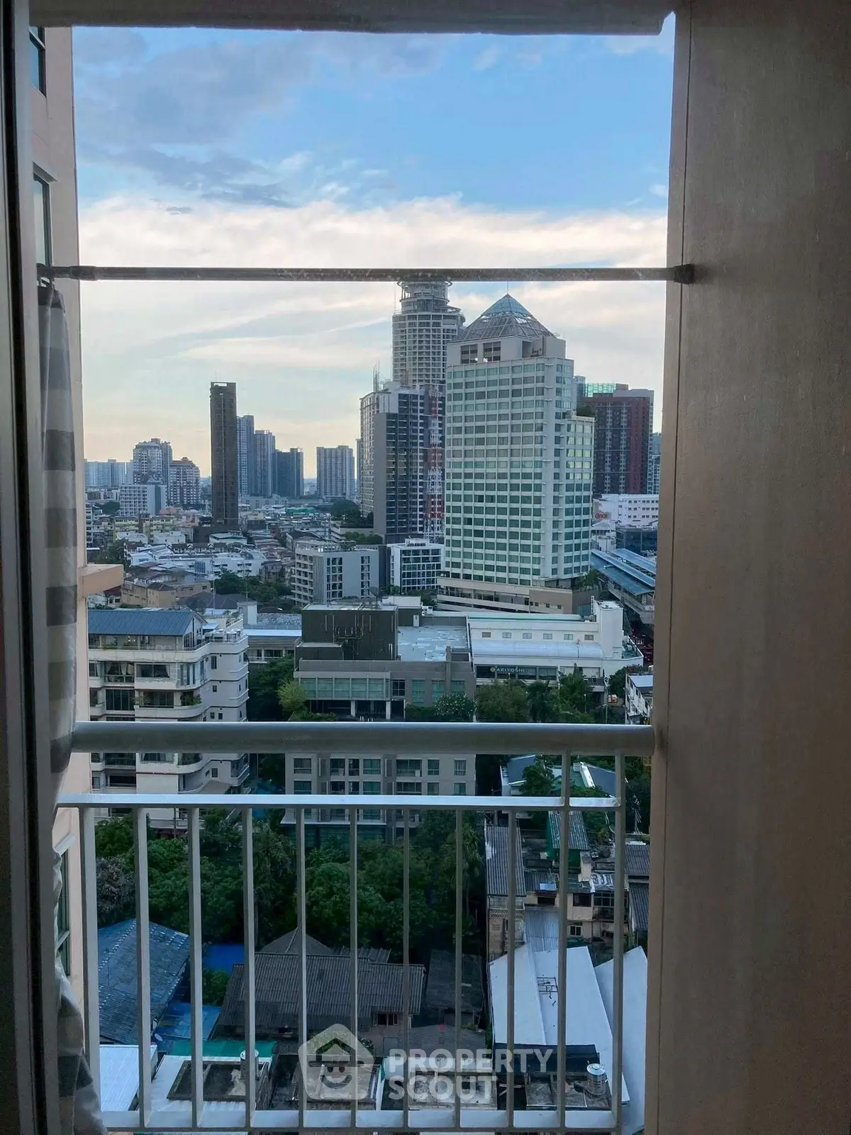 Stunning city view from high-rise balcony with urban skyline and lush greenery.
