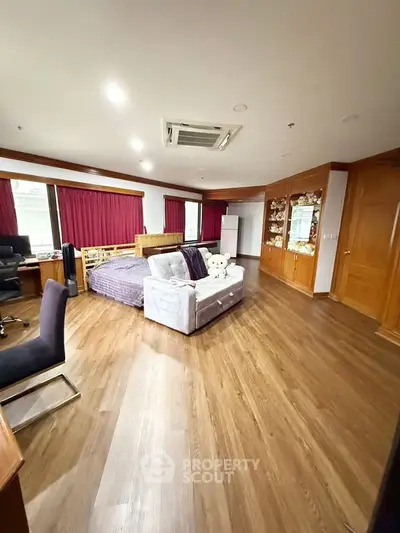 Spacious bedroom with wooden flooring, cozy bed, and elegant furnishings in a luxurious apartment.
