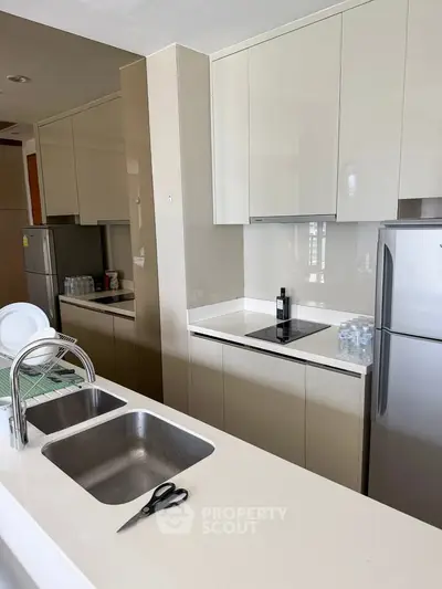 Modern kitchen with sleek cabinetry and built-in appliances, featuring a stylish countertop and stainless steel fridge.
