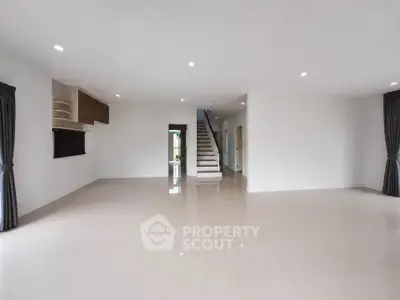 Spacious open-plan living room with modern staircase and elegant tiled flooring.