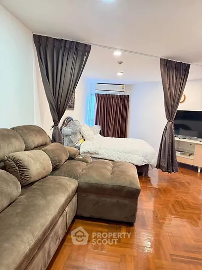 Cozy living room with plush sofa and bed, featuring elegant curtains and wooden flooring.