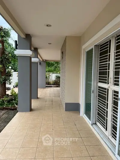 Spacious covered patio with tiled flooring and garden view, perfect for outdoor relaxation.