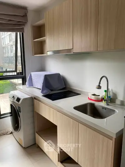 Modern kitchen with sleek cabinetry and built-in washing machine, featuring a compact layout and large window.