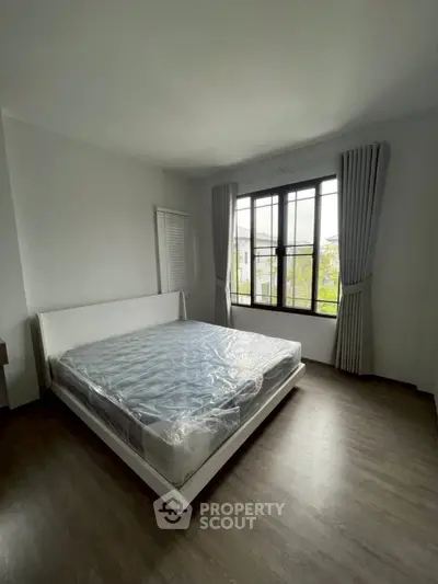 Spacious bedroom with large window and modern bed frame, offering natural light and a serene atmosphere.