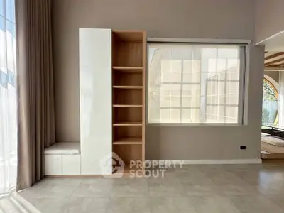 Modern living room with built-in shelving and large window, featuring elegant curtains and neutral tones.
