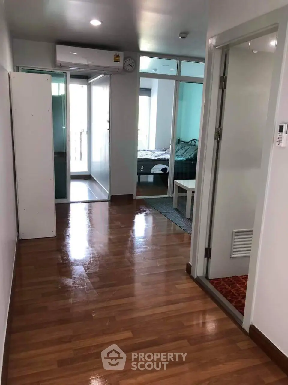 Spacious apartment hallway leading to a cozy bedroom with wooden flooring and modern decor.