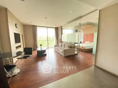 Spacious modern living room with wooden flooring and glass partition leading to bedroom.