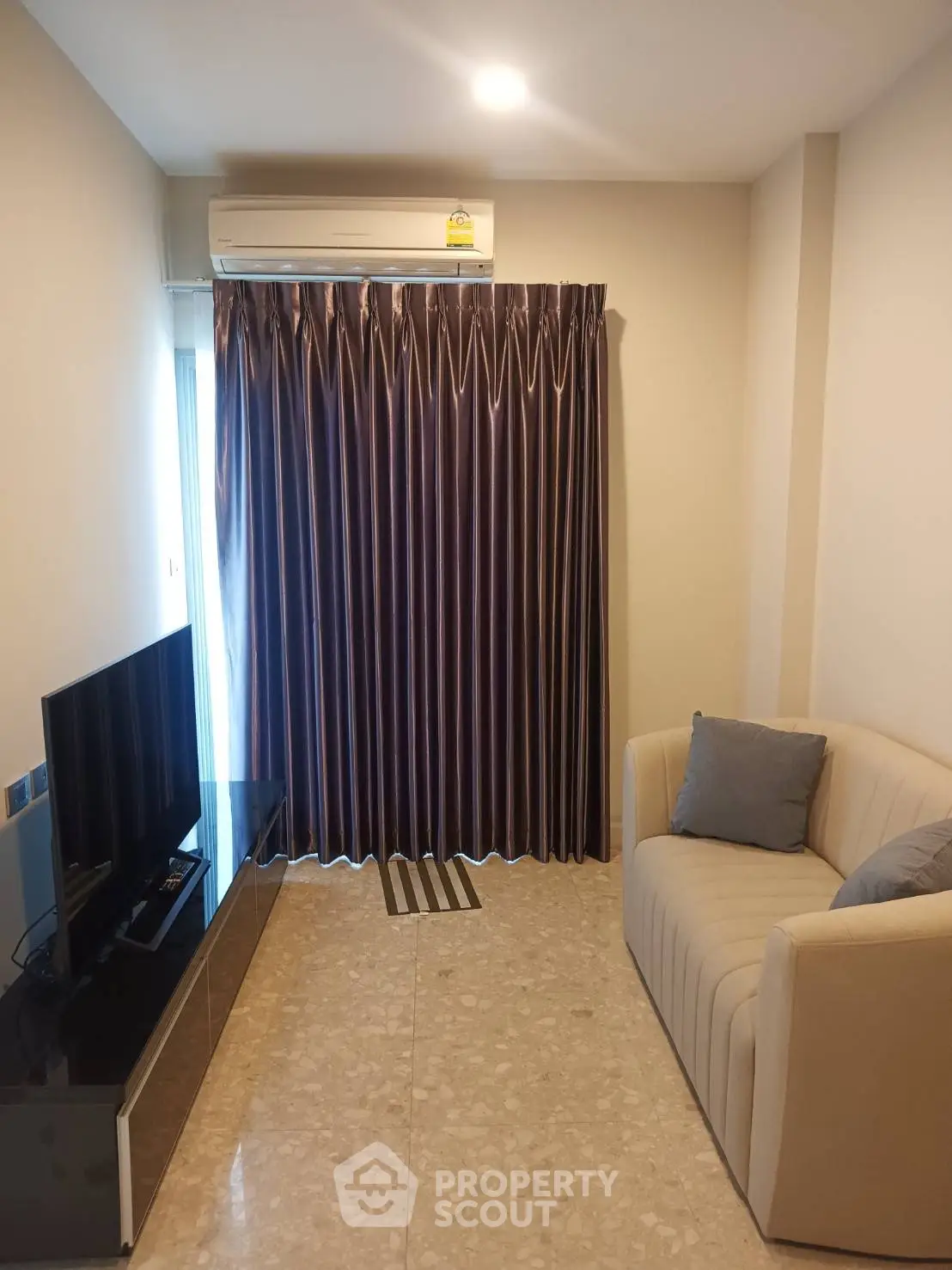 Cozy living room with modern sofa and TV, featuring elegant curtains and air conditioning.