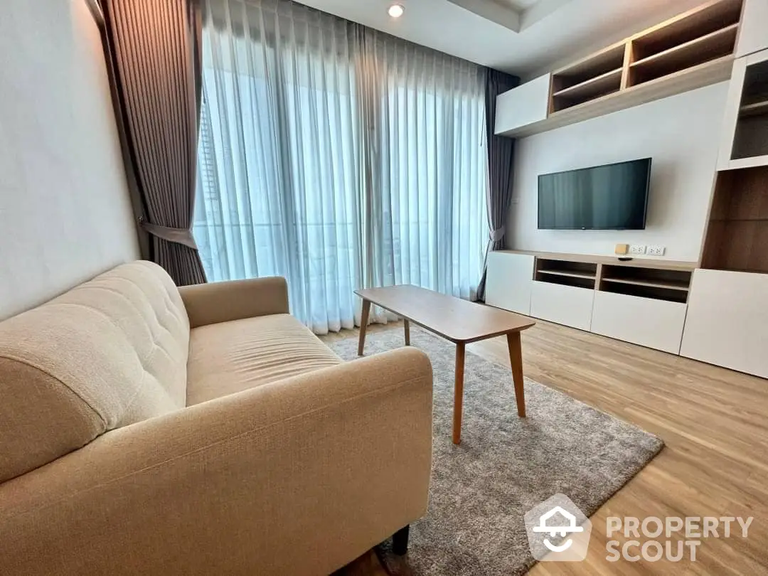 Spacious and modern living room with plush sofa, elegant entertainment unit, and large windows draped with sheer curtains, perfect for urban living.