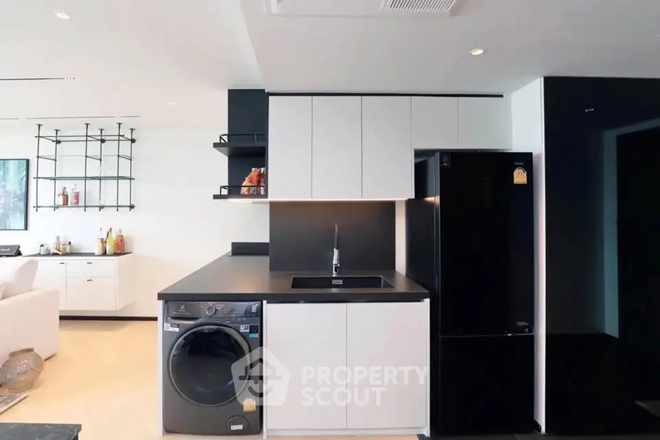 Modern kitchen with sleek black and white cabinetry, featuring a washing machine and refrigerator.