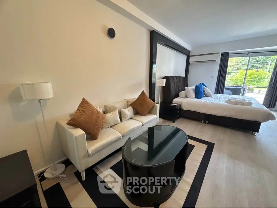 Spacious studio with modern decor and large windows opening to a lush green view.