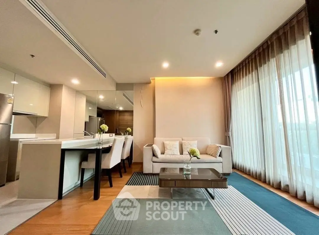 Modern living room with open kitchen, stylish decor, and large windows for natural light.