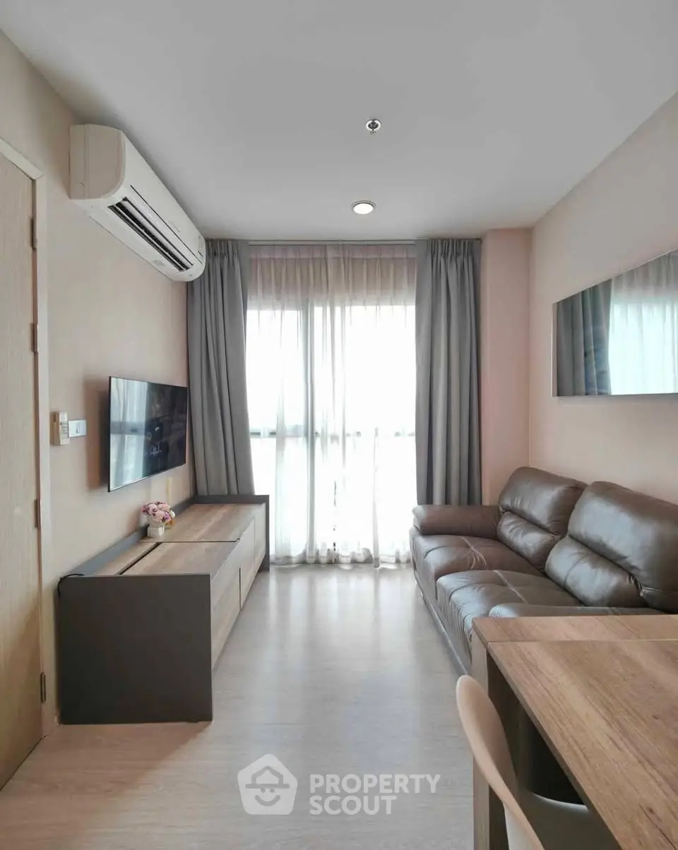 Modern living room with leather sofa and wall-mounted TV, featuring natural light from large window.