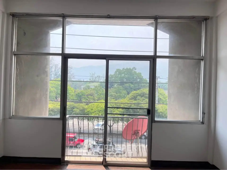 Spacious apartment with large windows offering a scenic view of lush greenery and urban landscape.