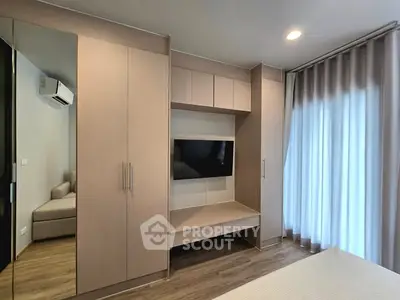 Modern bedroom with built-in wardrobe and TV, featuring sleek design and natural light.
