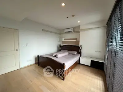 Spacious bedroom with wooden flooring and elegant bed frame, featuring natural light through large windows.