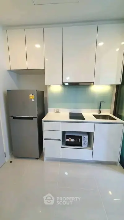 Modern kitchen with sleek white cabinets, built-in appliances, and a compact fridge in a stylish apartment.