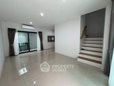 Spacious modern living room with sleek tile flooring and staircase, featuring large windows and natural light.