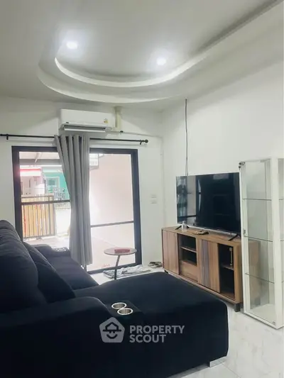 Modern living room with sleek black sofa, wall-mounted TV, and stylish ceiling design.