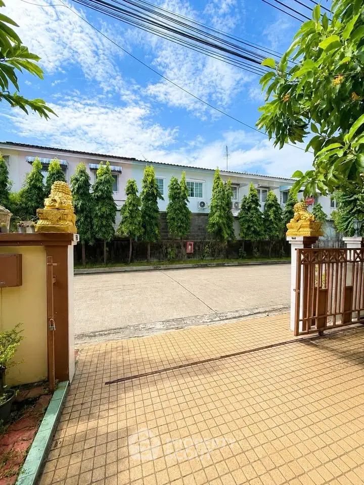 Charming residential entrance with paved driveway and lush greenery under a clear blue sky.