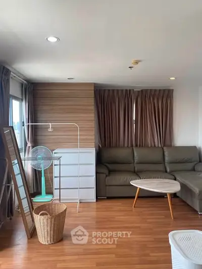 Spacious living room with modern decor and natural light, featuring a cozy sofa and stylish wooden flooring.