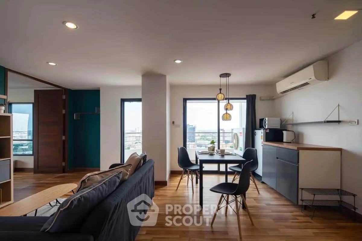 Modern open-plan living room with dining area and city view, featuring sleek furniture and wooden flooring.