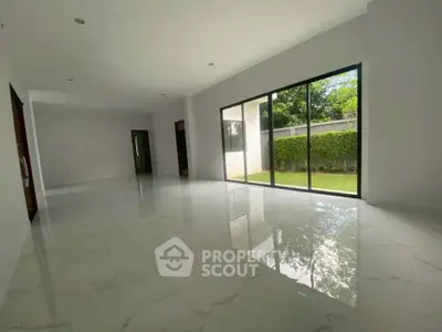 Spacious modern living room with large windows and garden view, featuring sleek marble flooring.