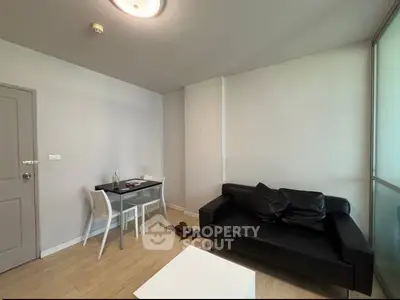 Modern living room with sleek black sofa and minimalist dining area in a cozy apartment.