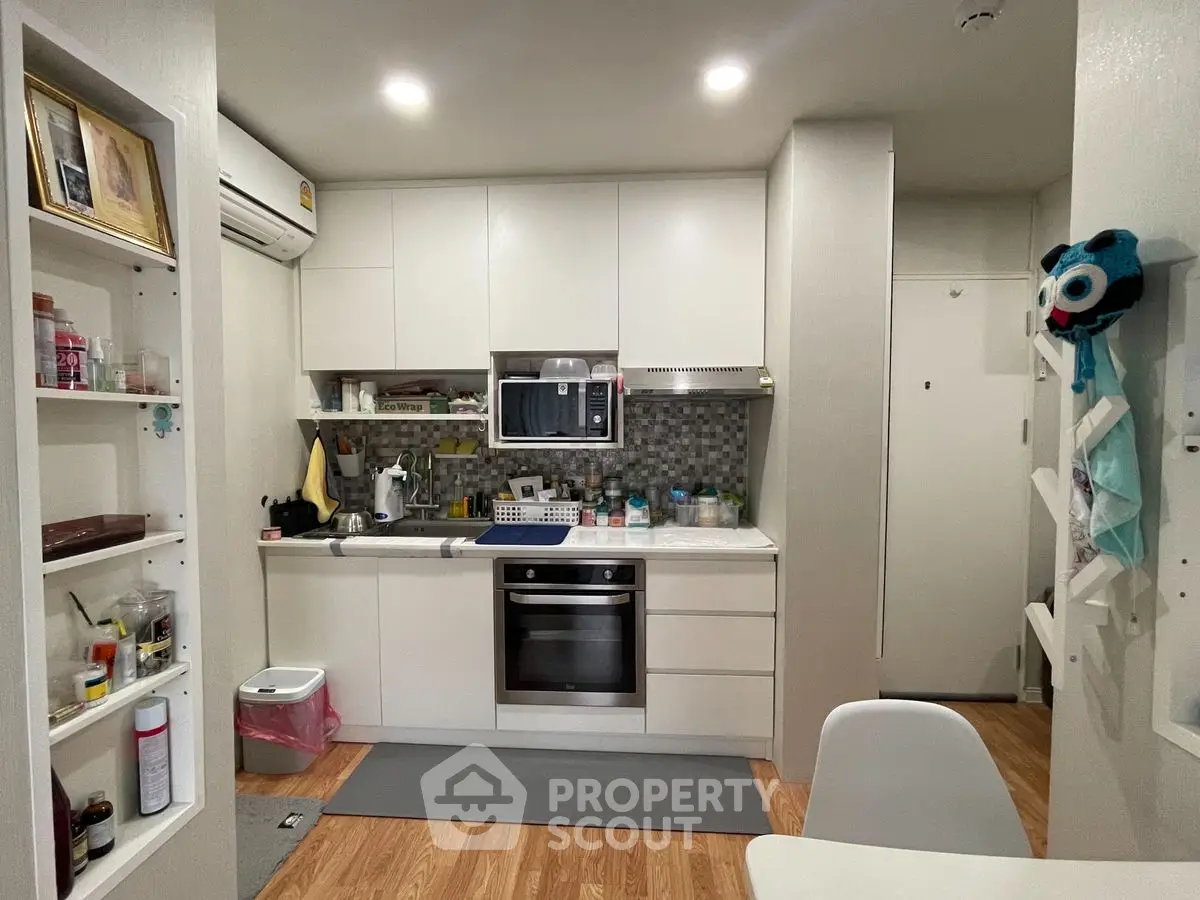 Modern kitchen with sleek white cabinets and built-in oven in cozy apartment
