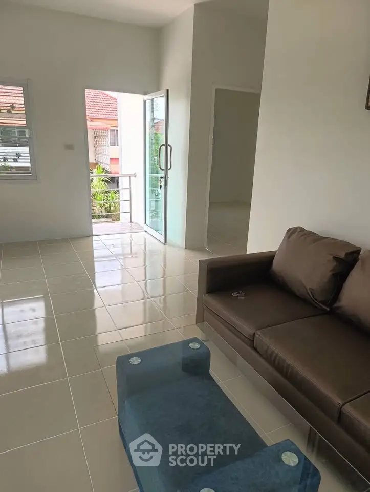 Spacious living room with modern sofa and glass table, leading to a balcony with a view.