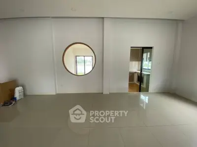 Spacious modern living room with unique circular window and open kitchen view.